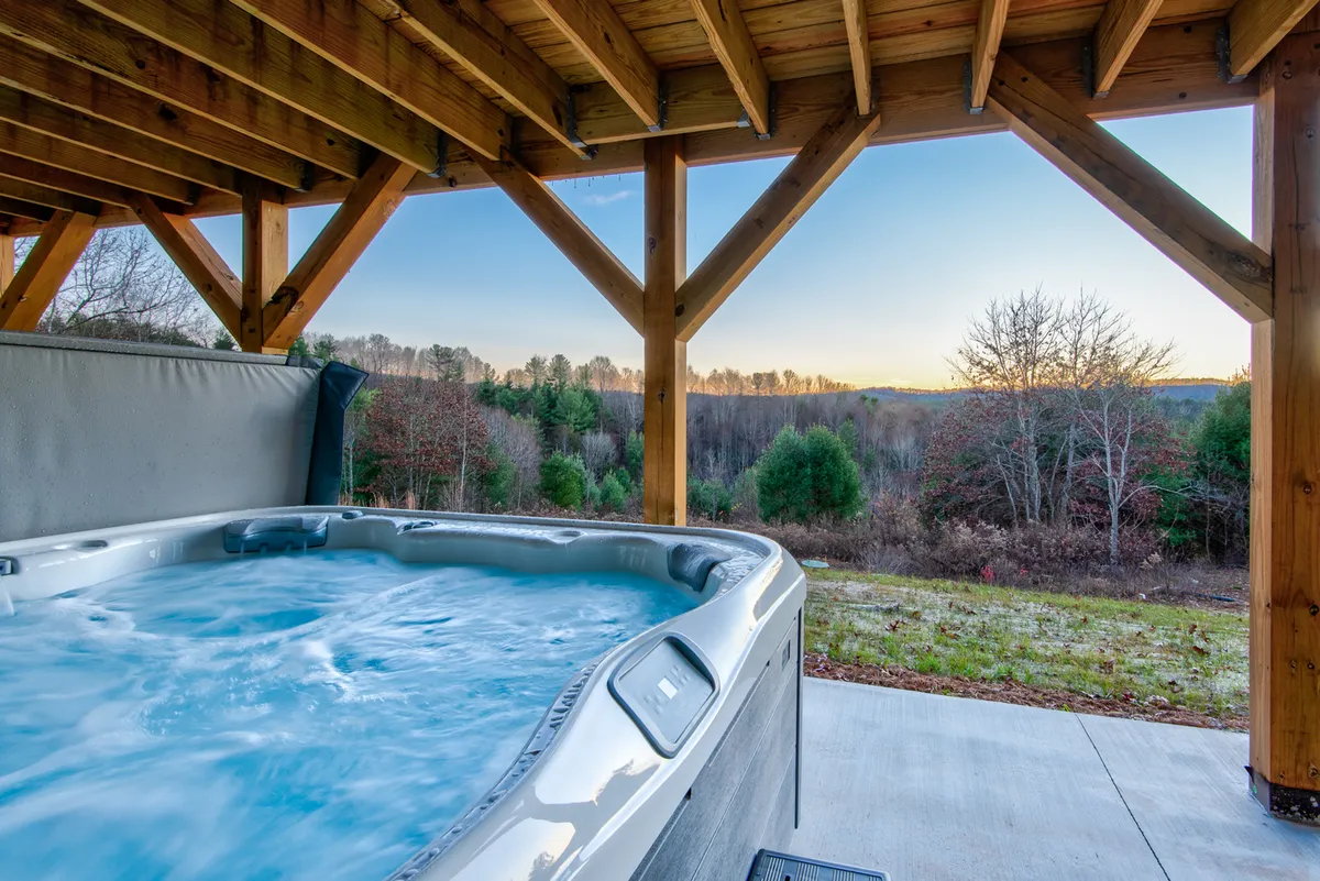This exterior image showcases a hot tub framed by wooden beams and offering views of the surrounding landscape. The area is designed for both relaxation and socializing, whether unwinding after river excursions or soaking under the stars as a family.