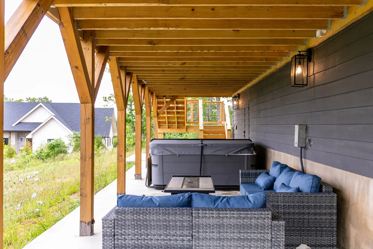 This image showcases a relaxing outdoor hot tub surrounded by comfortable seating and wooden beams, set against a natural backdrop. The area looks perfect for groups to gather, unwind, and enjoy time together under the stars.