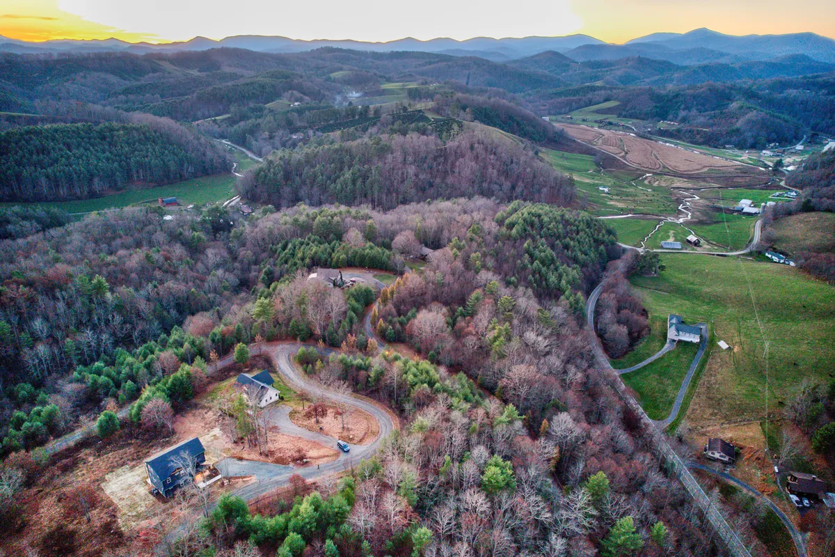 A scenic panorama showing rolling hills, a curved road winding through the dense forest, and scattered houses. The setting sun paints the landscape in warm light, inviting exploration and promising wildlife sightings and peaceful retreats.