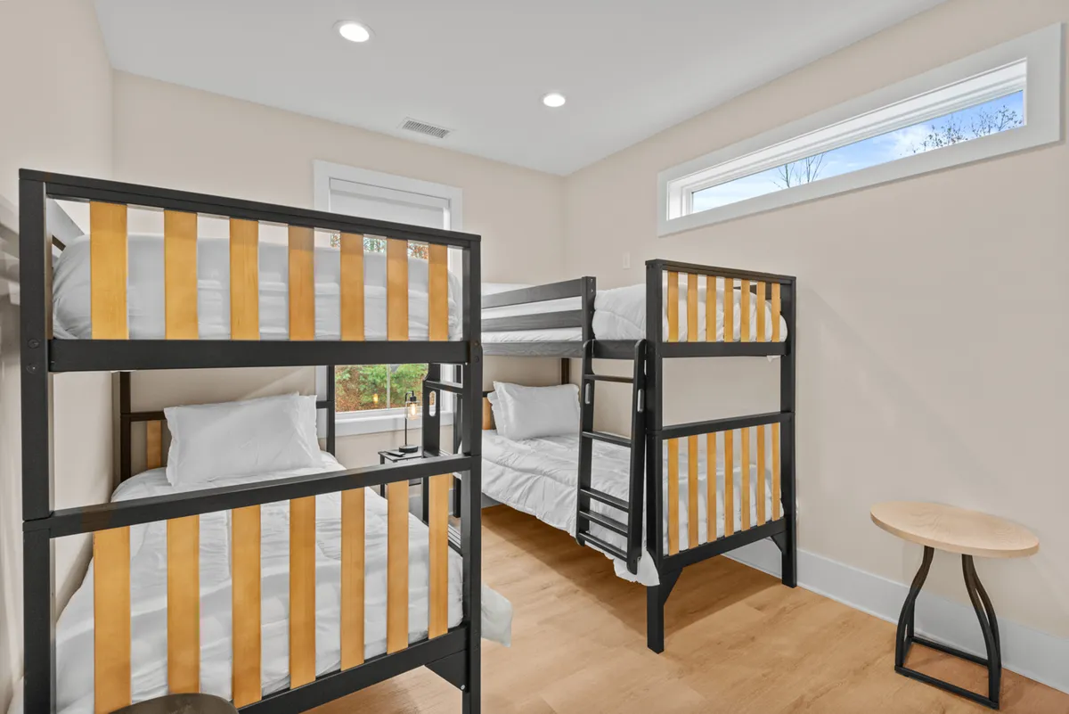 A cheerful bunk room with double wooden bunk beds, a side table, and playful natural light streaming in from the windows. The space exudes a sense of fun, togetherness, and comfort—perfect for children or friends sharing the space.