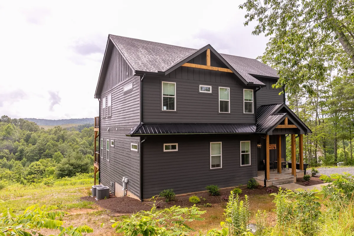 The house’s charming exterior is framed by lush greenery and features a welcoming porch entrance. The scene captures the sense of arriving at a secluded, resort-style mountain retreat—inviting guests to begin their immersive work escape experience.