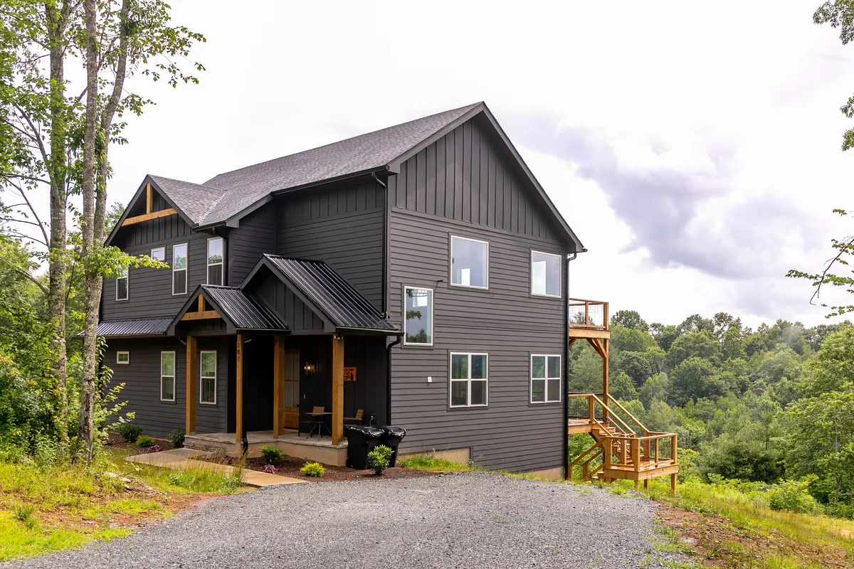 This image features the modern exterior architecture of Gabby's Getaway, a spacious wooden deck, and lush surrounding trees. The deck is designed for outdoor gatherings and relaxation, with ample space for family members to enjoy nature or share meals together. The soft sunset lighting creates a peaceful and welcoming mood, perfect for families coming together after a day of adventure.