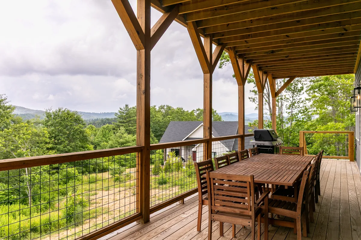 This image highlights a wooden deck set for outdoor dining, with a family-sized table, a barbecue grill, and views of the surrounding wilderness. The setup is perfect for group barbecues, morning coffees, or celebratory meals, set against a backdrop of trees and mountain air.