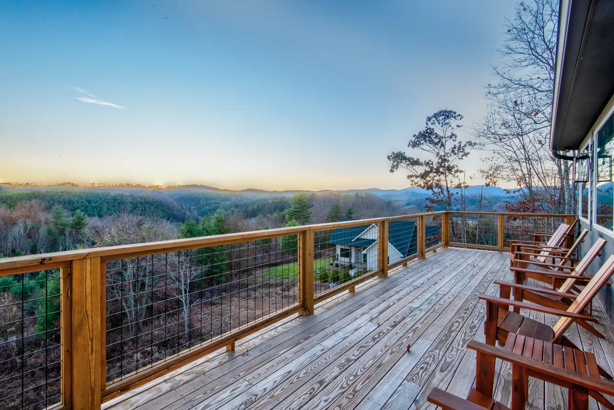 A serene deck furnished with wooden chairs overlooks sweeping mountain views under a vast sky. The setup suggests an inviting spot for group brainstorming, casual team chats, or quiet moments of reflection, with the natural landscape providing a beautiful backdrop.